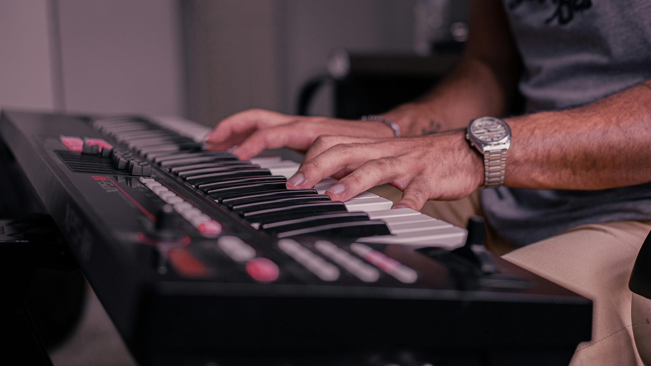 A musician's hands playing a keyboard indoors, creating music.